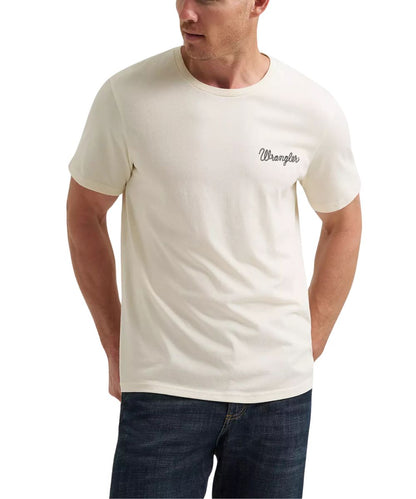 A man wearing a cream-colored Wrangler short-sleeve t-shirt with the brand name printed in script on the left chest, paired with dark blue jeans against a plain white background.