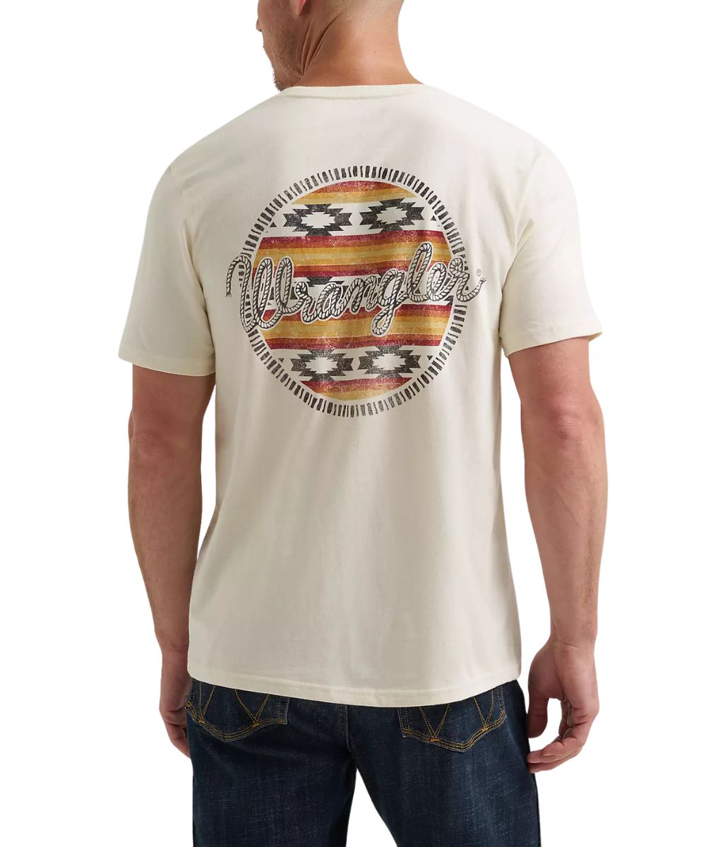 A man wearing a cream-colored Wrangler t-shirt, viewed from the back. The shirt features a large circular graphic on the back with a distressed Southwestern-style pattern in red, orange, yellow, and black, with the brand name 'Wrangler' written across the center in white script.