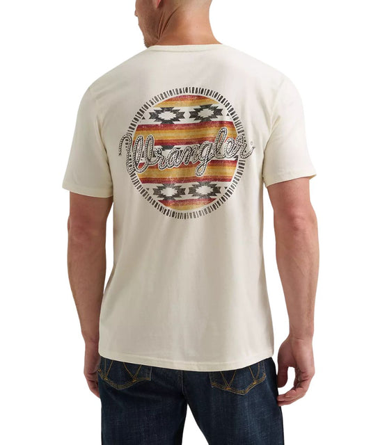 A man wearing a cream-colored Wrangler t-shirt, viewed from the back. The shirt features a large circular graphic on the back with a distressed Southwestern-style pattern in red, orange, yellow, and black, with the brand name 'Wrangler' written across the center in white script.