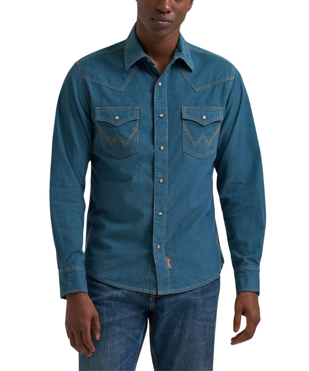 A man wearing a blue corduroy long-sleeve western shirt with contrast stitching and chest pockets, paired with blue jeans, against a plain white background.