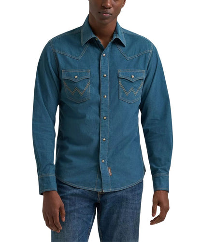 A man wearing a blue corduroy long-sleeve western shirt with contrast stitching and chest pockets, paired with blue jeans, against a plain white background.