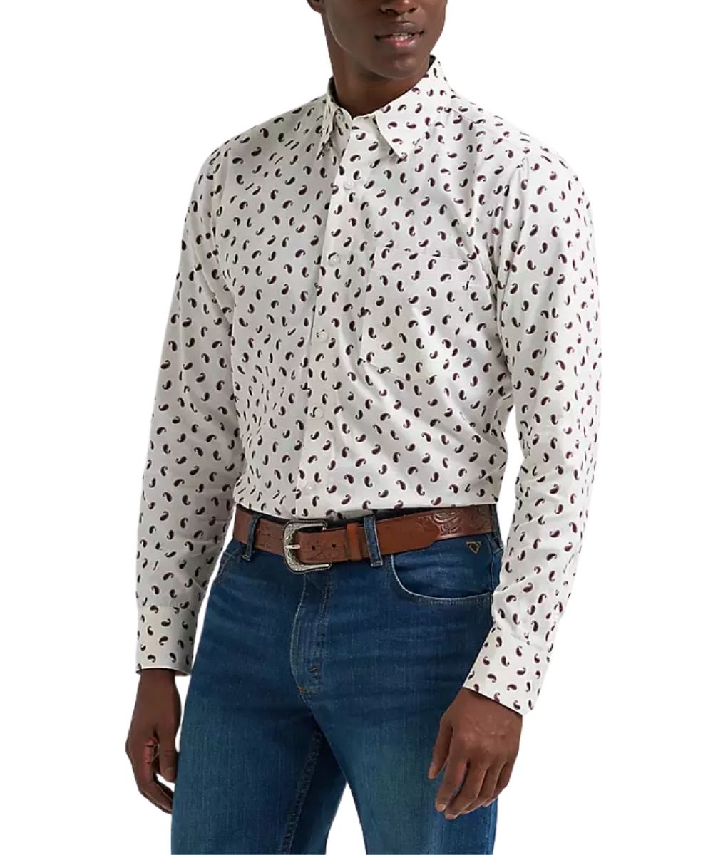 A man wearing a long-sleeve button-up shirt with a wine paisley pattern on an off-white background, paired with blue jeans and a brown leather belt, against a plain white studio background.
