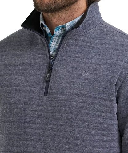 A close-up of a man wearing a heathered slate blue-gray quarter-zip pullover sweater with a black collar, layered over a blue and white plaid button-down shirt.