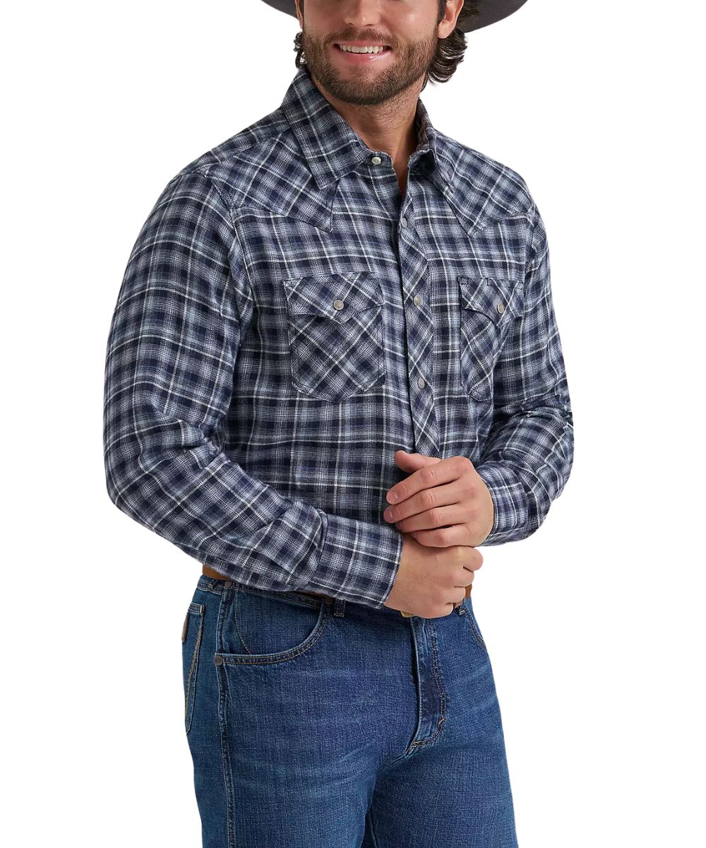 A man wearing a long-sleeve western plaid button-down shirt in navy, gray, and white, paired with blue jeans against a white studio background.
