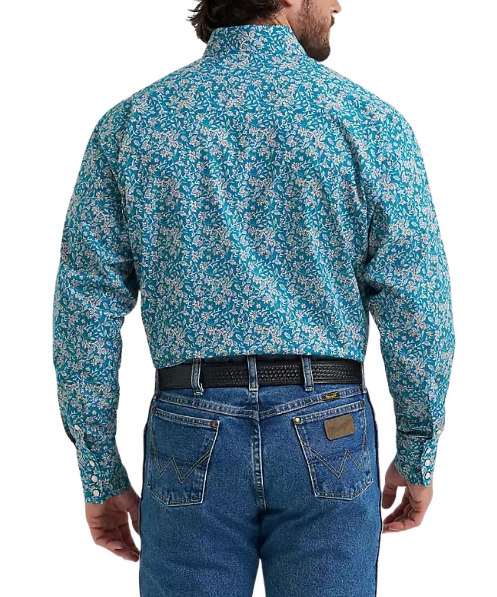 A man viewed from the back wearing a long-sleeve button-down shirt with a dense blue, teal, and white floral pattern, tucked into blue jeans with a black belt.