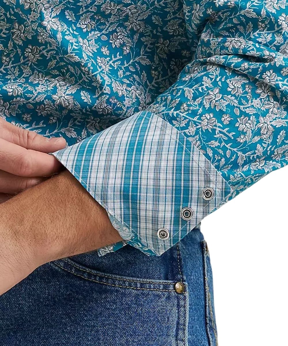 Close-up of a person wearing a blue and white floral long-sleeve shirt with a plaid turned-back cuff, paired with blue jeans.