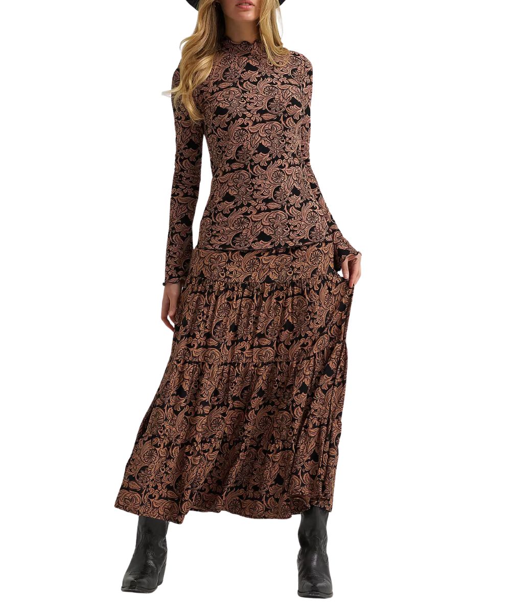 A woman modeling a long-sleeve, high-neck maxi dress with a brown and black paisley pattern, paired with black ankle boots against a plain white background.