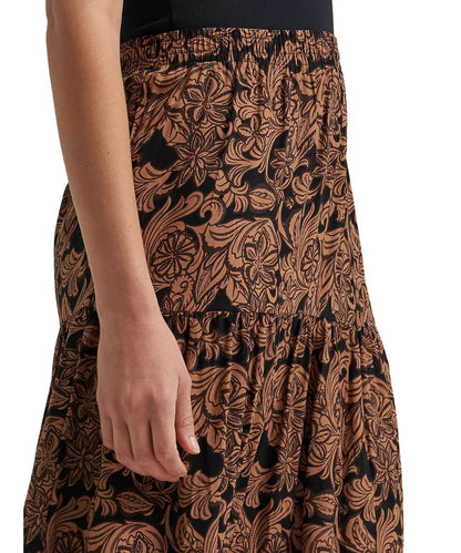 Close-up of a person wearing a black skirt with a brown floral and scroll pattern, showing the side and hand area against a plain white background.