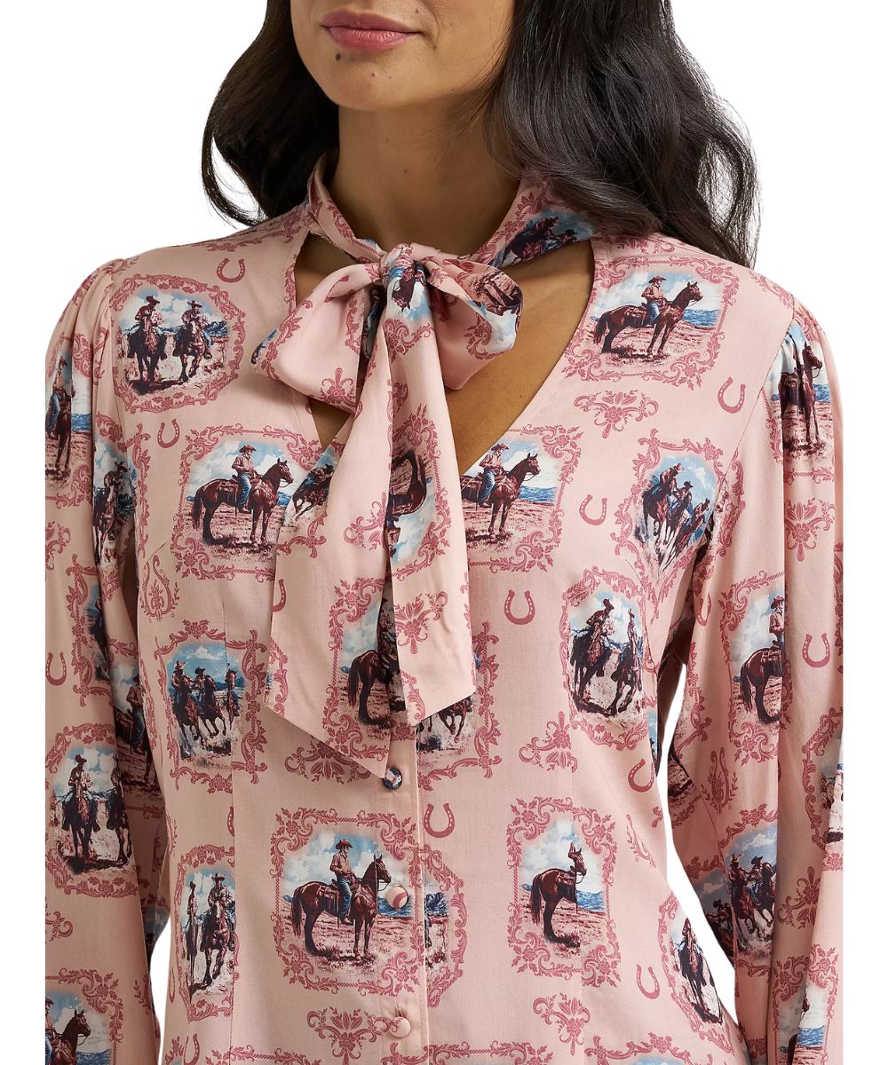 Close-up view of the women's pink blouse featuring the v-neckline with front tie, the button front closure, and puff sleeves