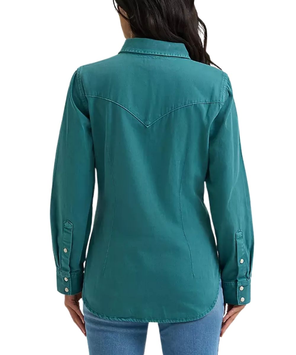 A woman viewed from the back wearing a teal long-sleeve western-style button-up shirt with a pointed collar and decorative stitching, paired with blue jeans against a plain white background.