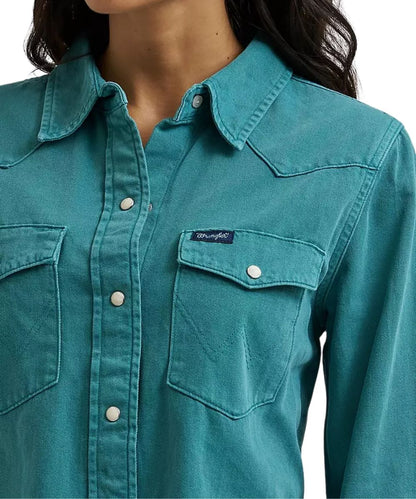 A close-up of a woman wearing a teal western-style button-up shirt with two chest pockets and a visible Wrangler label on the left chest pocket.