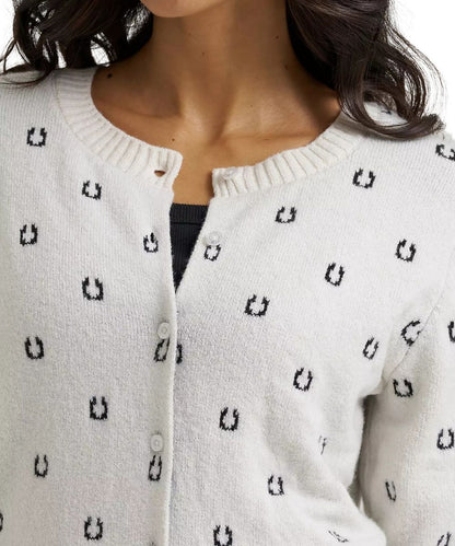 Close-up of a person wearing a cream knit cardigan with a repeating black horseshoe pattern, shown from the shoulders to the chest.