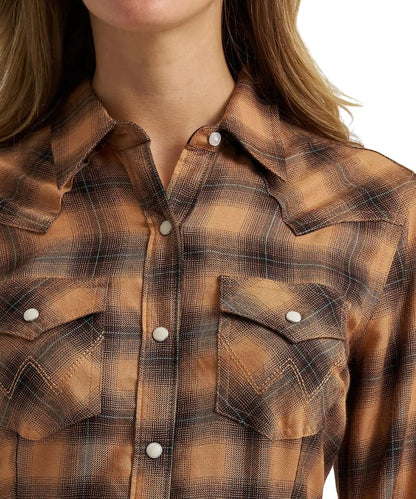 Close-up of a woman wearing a brown and tan plaid western-style button-up shirt with white snap buttons and chest pockets.