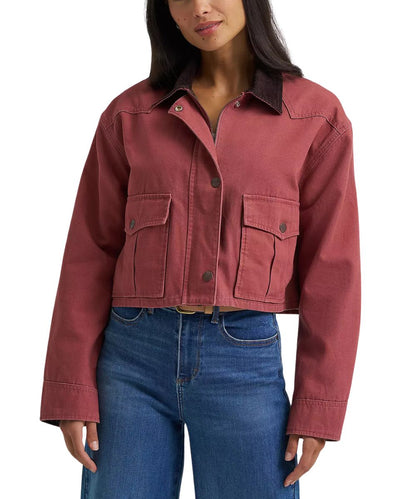 A woman wearing a cropped dusty rose utility jacket with dark brown corduroy collar and blue jeans, shown from the nose down against a plain white background.