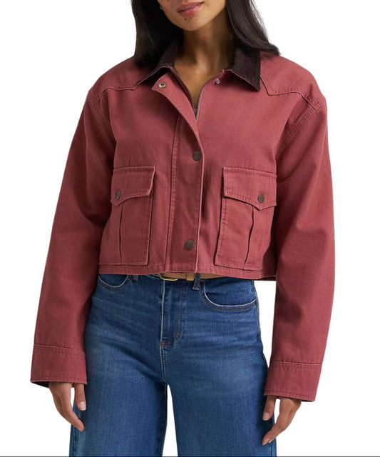 A woman wearing a cropped dusty rose utility jacket with dark brown corduroy collar and blue jeans, shown from the nose down against a plain white background.