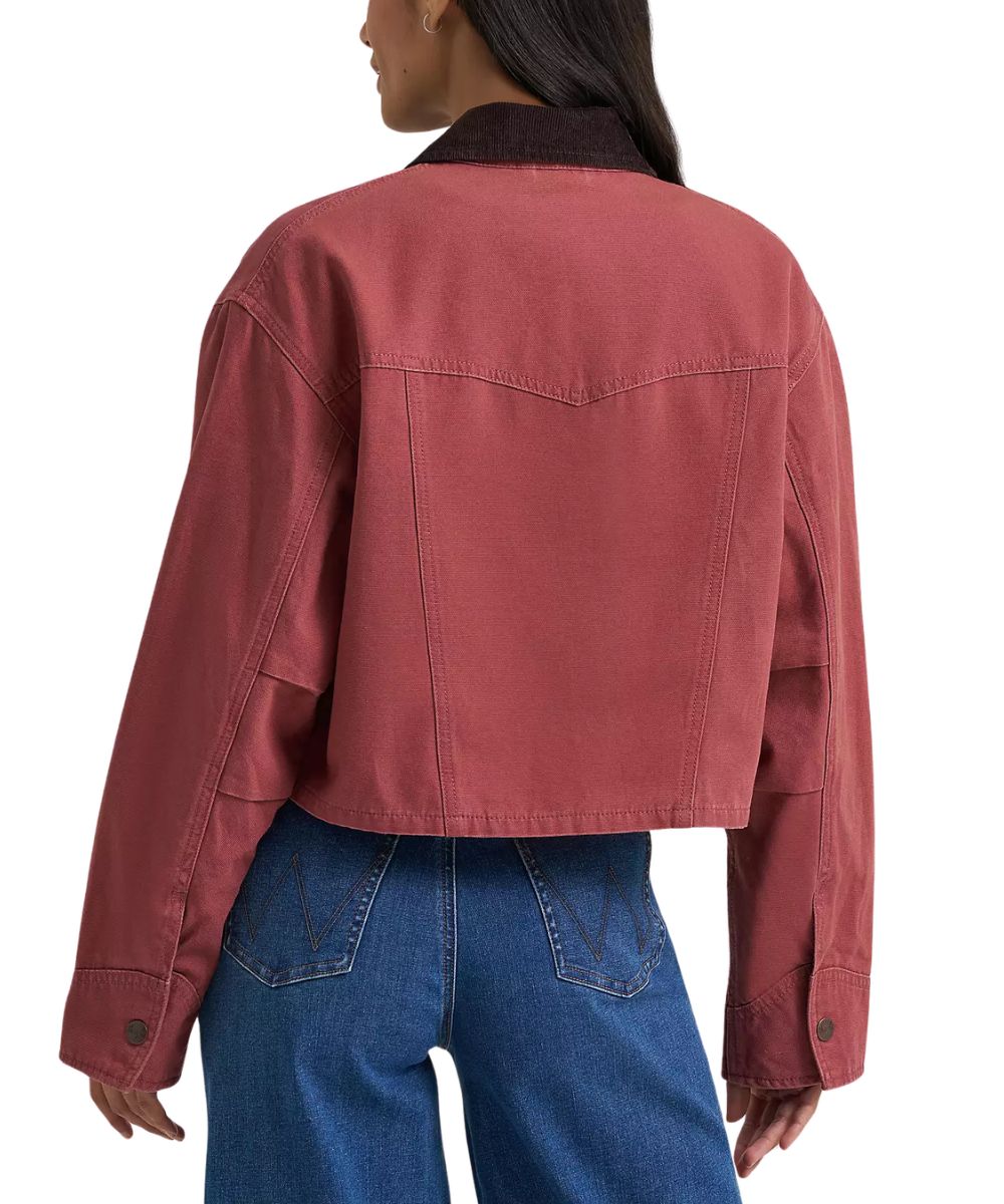 A woman from behind wearing a cropped dusty rose utility jacket with dark brown corduroy collar and blue jeans against a plain white background.