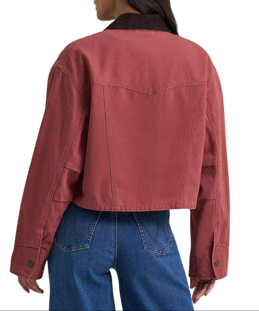 A woman from behind wearing a cropped dusty rose utility jacket with dark brown corduroy collar and blue jeans against a plain white background.
