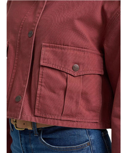 Close-up of a dusty rose utility jacket with a buttoned chest pocket, worn over blue jeans.