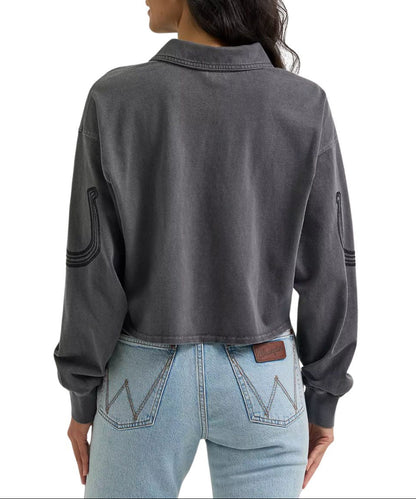 A woman shown from the back wearing a dark gray cropped long-sleeve shirt with decorative stitching on the sleeves and light blue jeans with contrast stitching.