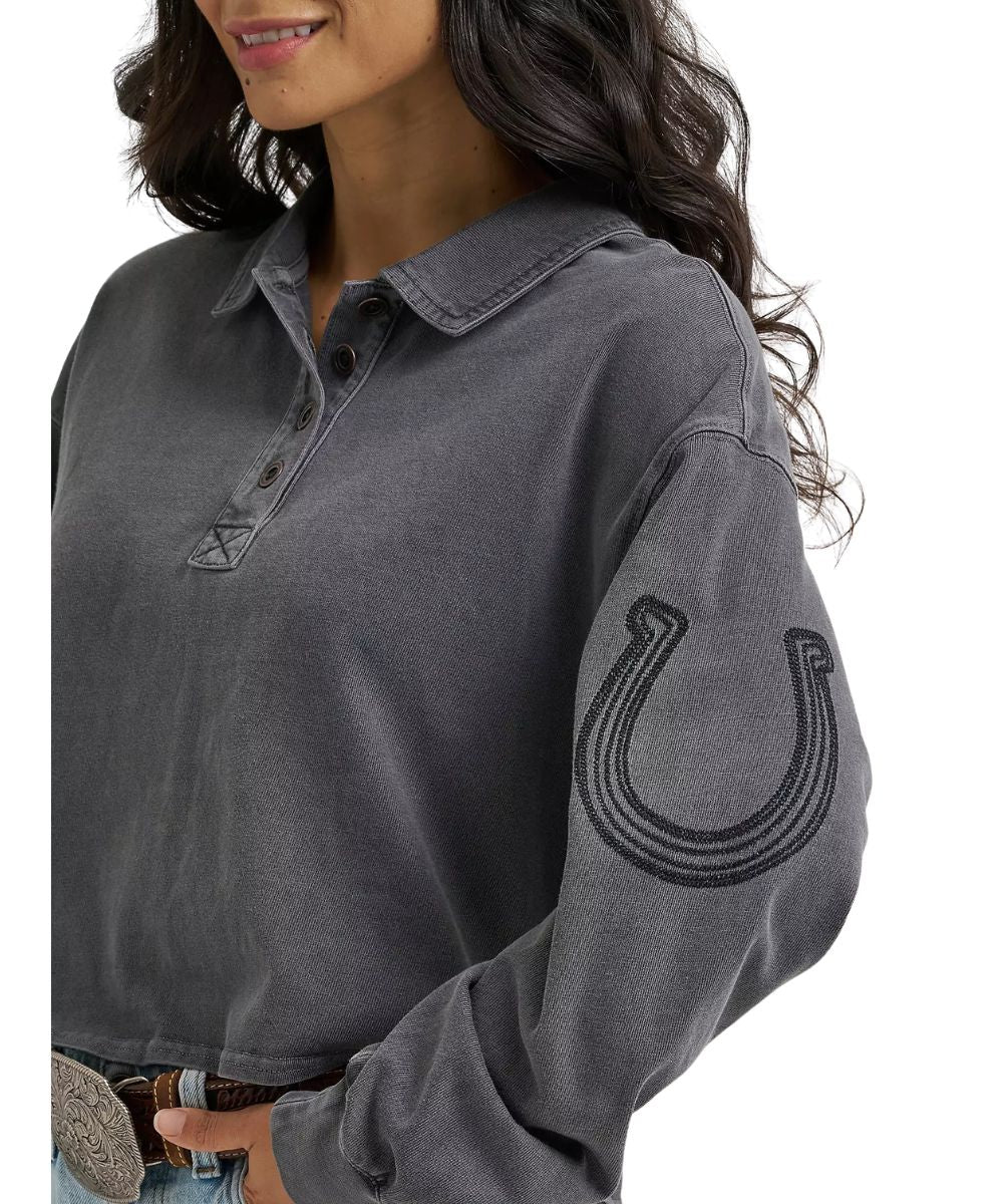 A woman wearing a dark gray long-sleeve henley shirt with a black embroidered horseshoe graphic on the sleeve, shown against a plain white background.