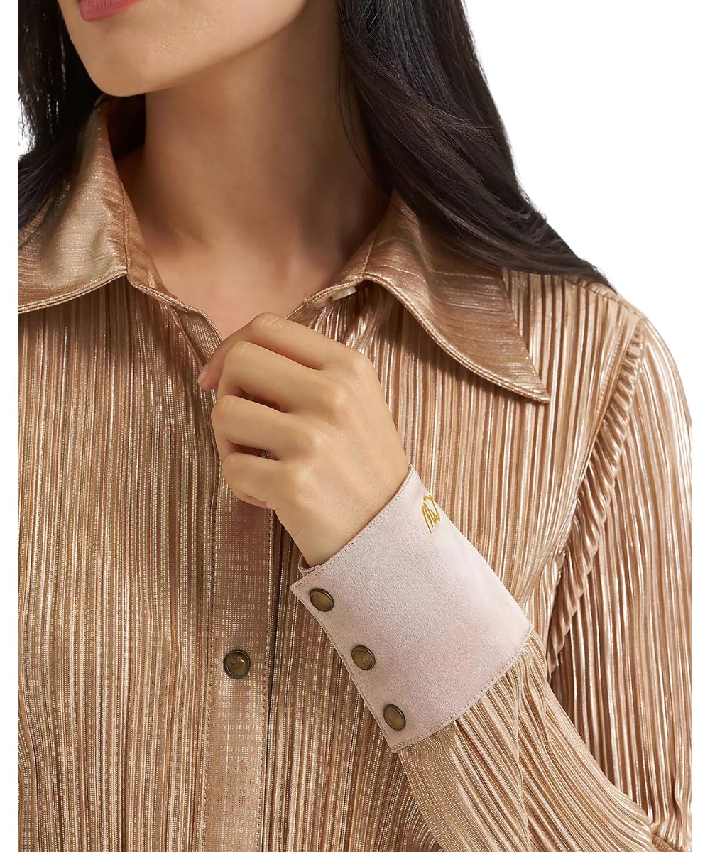Close-up of a woman wearing a metallic champagne pleated button-down shirt with a light pink cuff and gold buttons.