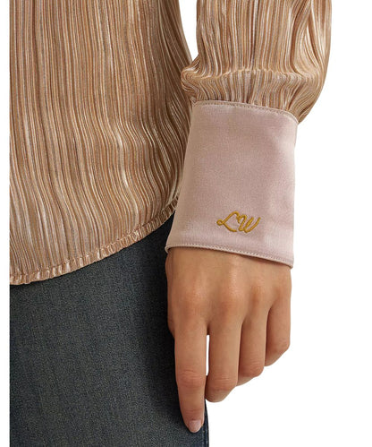 Close-up of a person wearing a champagne-colored pleated long-sleeve blouse with a light pink satin cuff featuring gold embroidered script.
