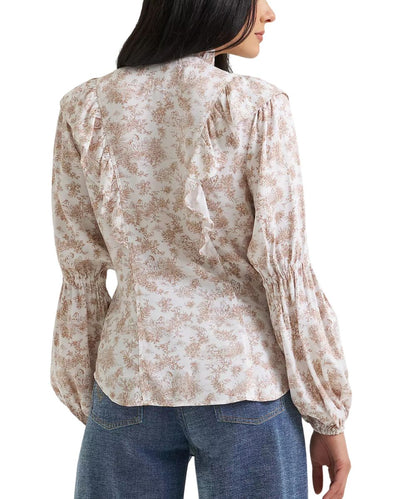 A woman shown from the back wearing a long-sleeve blouse with a beige and brown floral pattern, gathered ruffles at the shoulders, and elasticized cuffs, paired with blue jeans against a white background.