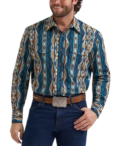 A man wearing a long-sleeve western-style button-up shirt with a blue, brown, and beige geometric pattern, paired with dark blue jeans and a brown belt with a silver buckle, against a plain white background.