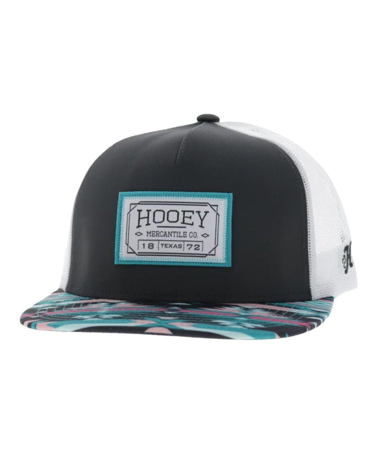 Left angled view of the unisex adult's Hooey Doc Trucker Cap featuring the charcoal front with a rectangle logo patch, the teal/charcoal/pink aztec hybrid bill, and white mesh sides 