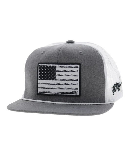 Left angled view of the unisex adult's Hooey Liberty Roper Trucker Cap featuring the grey front with a black/white American Flag liberty roper  rectangle patch, grey hybrid bill with a white brim rope, and white mesh sides