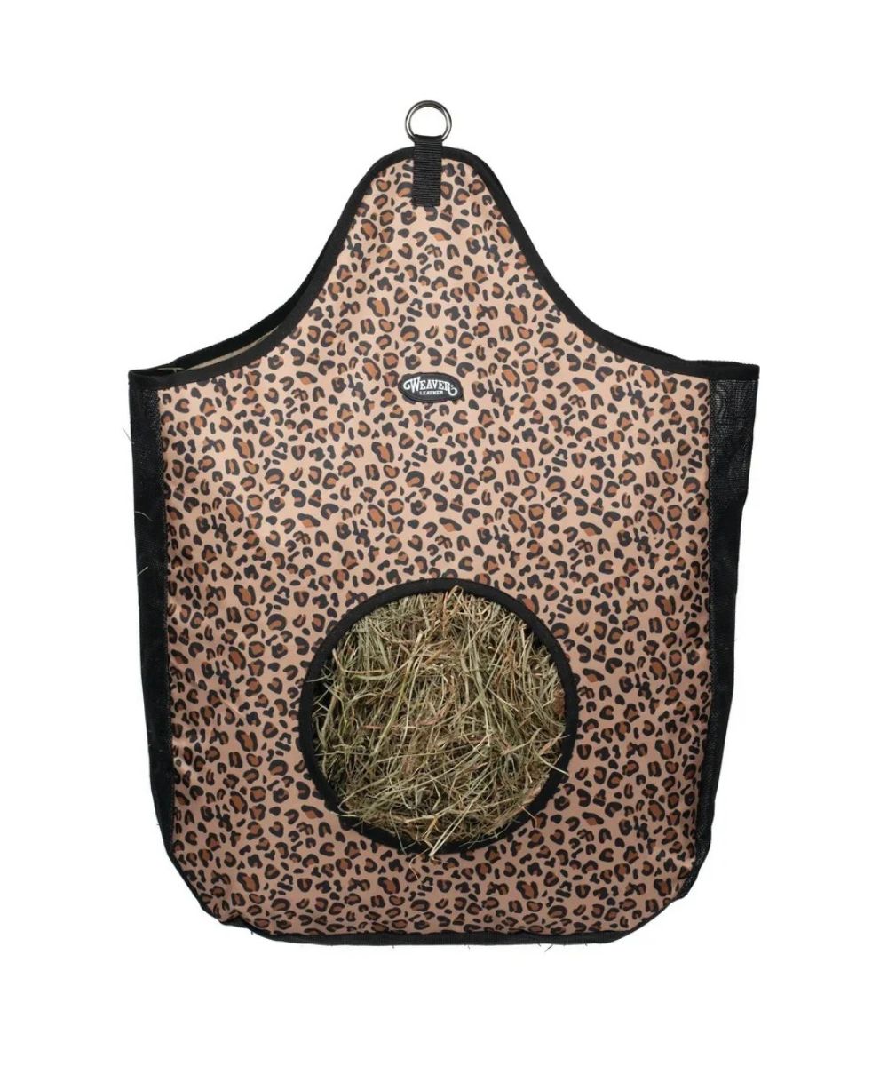 A leopard-print pet hanging feeder with a circular opening filled with hay, featuring black trim and a metal hanging ring at the top.