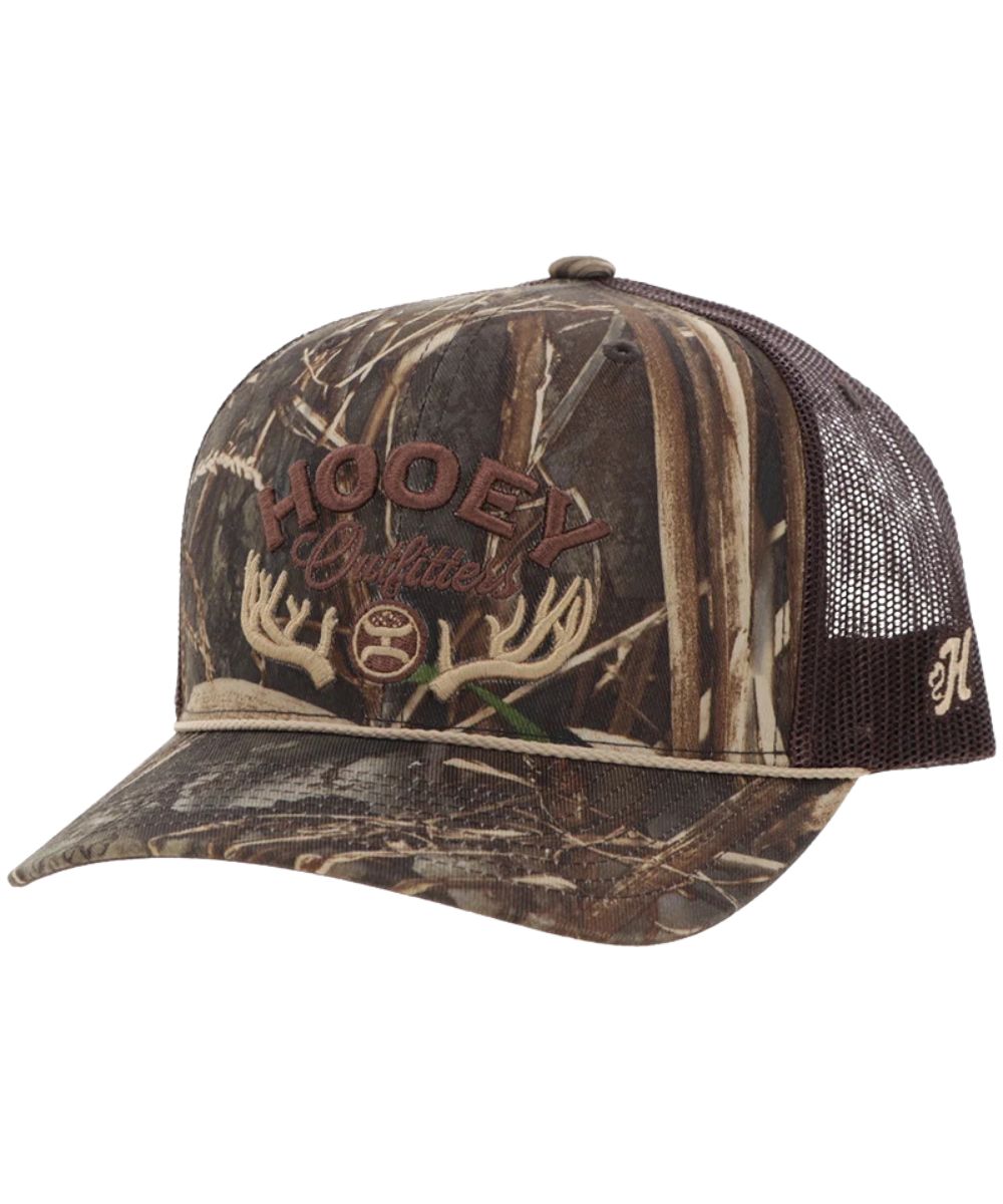 Left angled view of the unisex adult's Hooey Outfitters Cap featuring the Realtree Camo front with brown and tan logo embroidery and an antler graphic, Realtree Camo Curved bill with a tan brim rope, and brown mesh sides