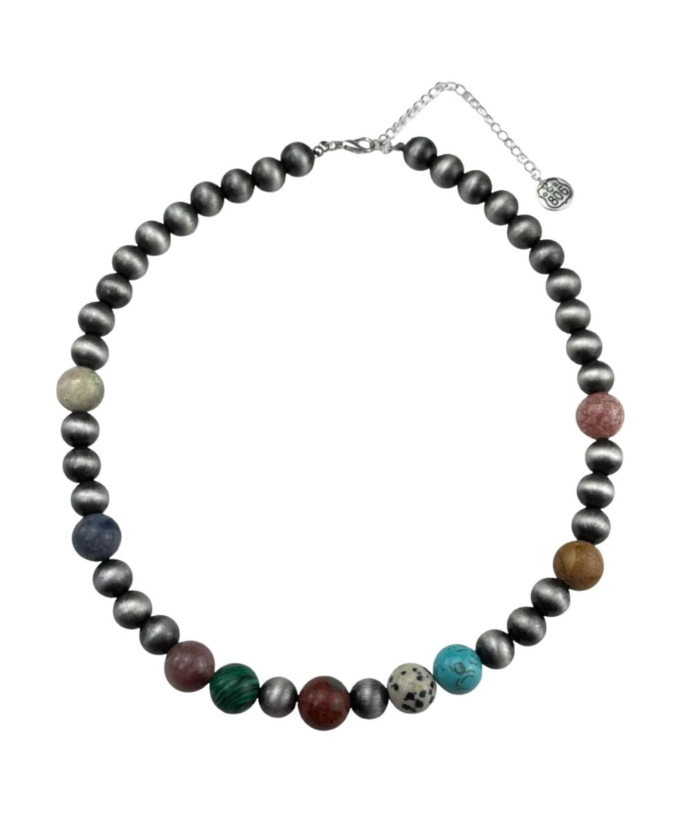 A beaded necklace featuring dark gray beads and a row of colorful accent stones in green, blue, pink, brown, and white, displayed on a clean white background.