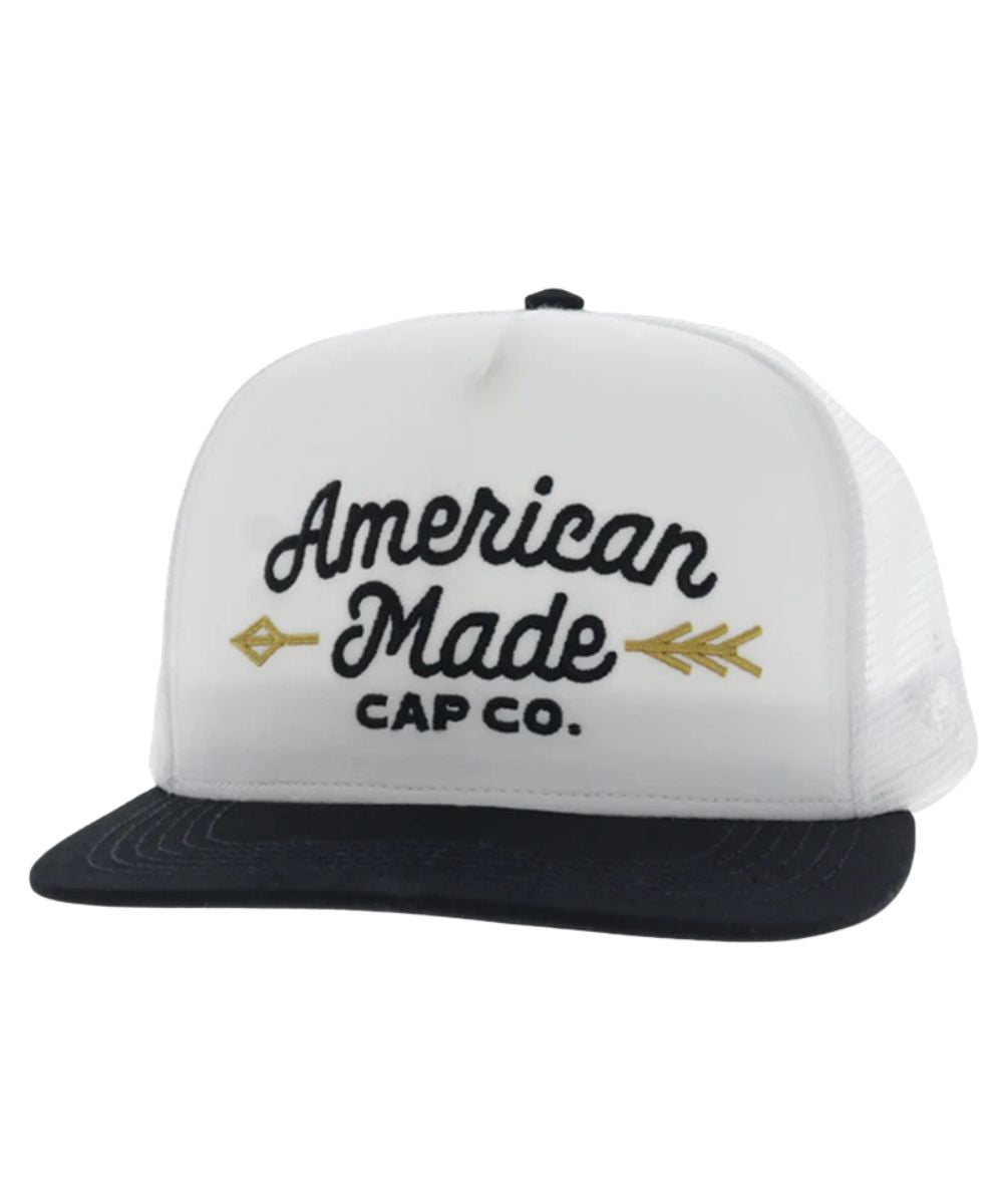 Left angled view of the unisex adult's Hooey American Made Cap Co. trucker cap featuring the white front with black logo stitching and a gold arrow, a black hybrid bill, and white mesh sides