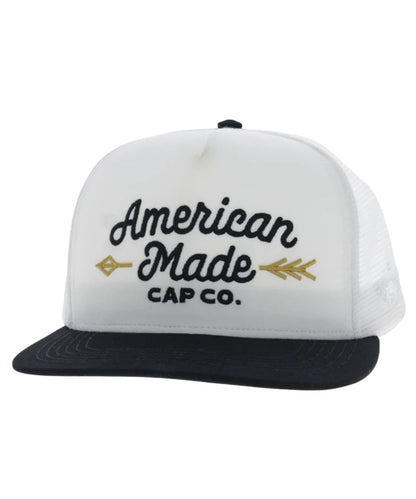 Left angled view of the unisex adult's Hooey American Made Cap Co. trucker cap featuring the white front with black logo stitching and a gold arrow, a black hybrid bill, and white mesh sides