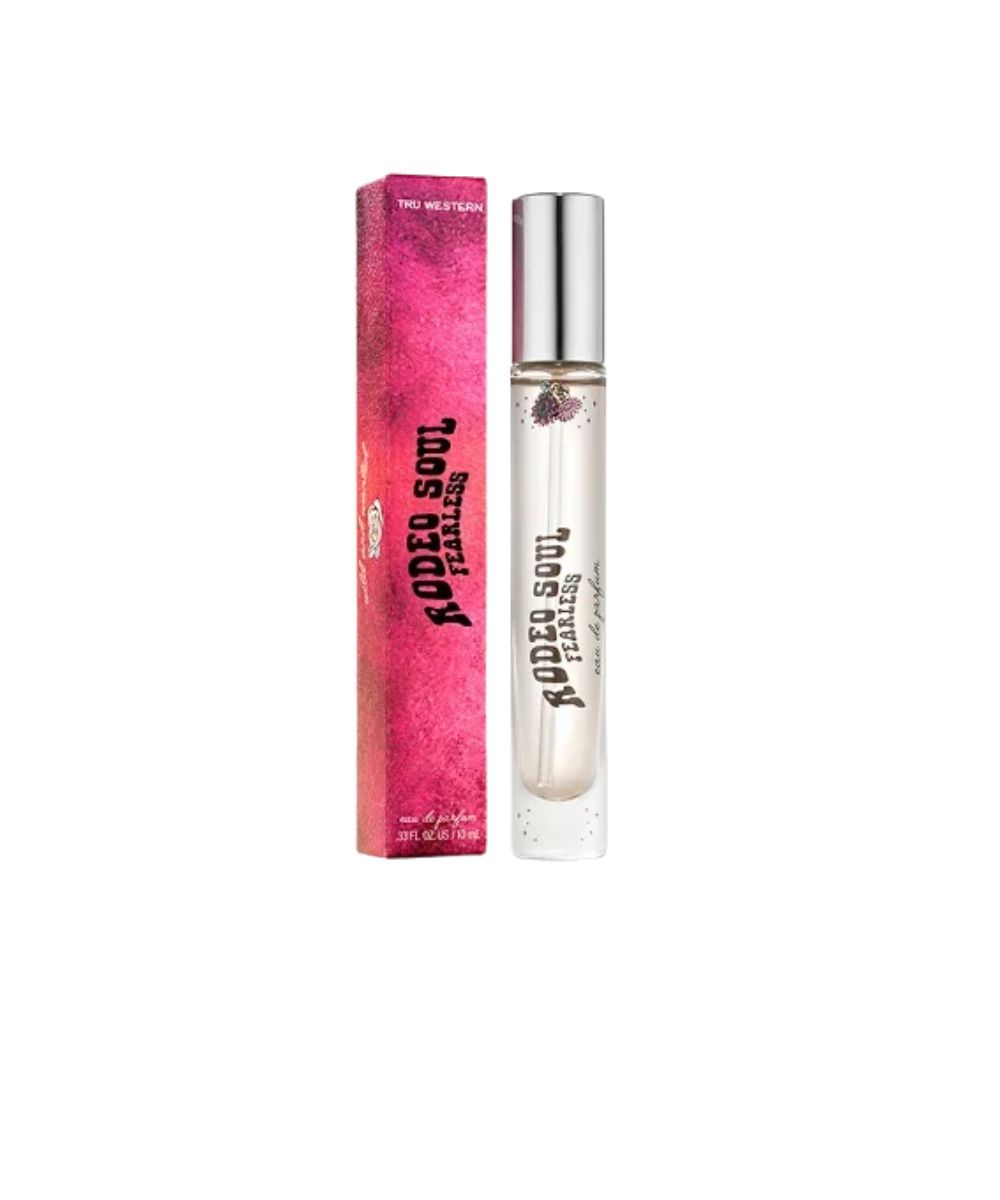 A clear cylindrical rollerball perfume bottle with a silver cap stands next to its bright pink packaging box. The box and bottle are printed with the text 'RODEO SOUL FEARLESS' in black.