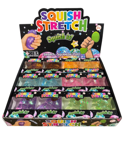 A retail display box filled with packaged squishy toys and glittery slime-like products under a large 'Squish Stretch' sign. The display contains multiple colors including purple, green, orange, pink, blue, and clear, with hands shown squeezing some items on the packaging and display board.