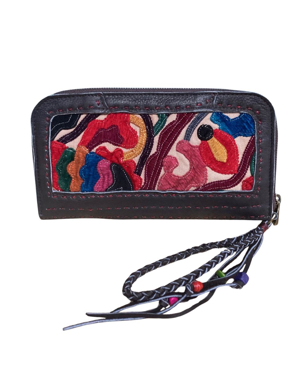 A brown leather zip-around wallet with a colorful embroidered floral panel on the back and a braided wrist strap and tassels with beads