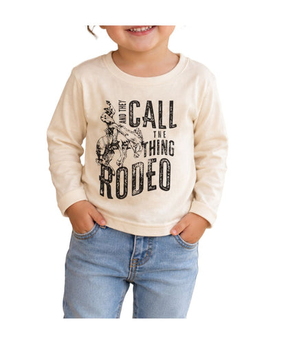 Model view of the toddler girl's beige long sleeve tee with a front screen print that reads: "and they call the thing rodeo"