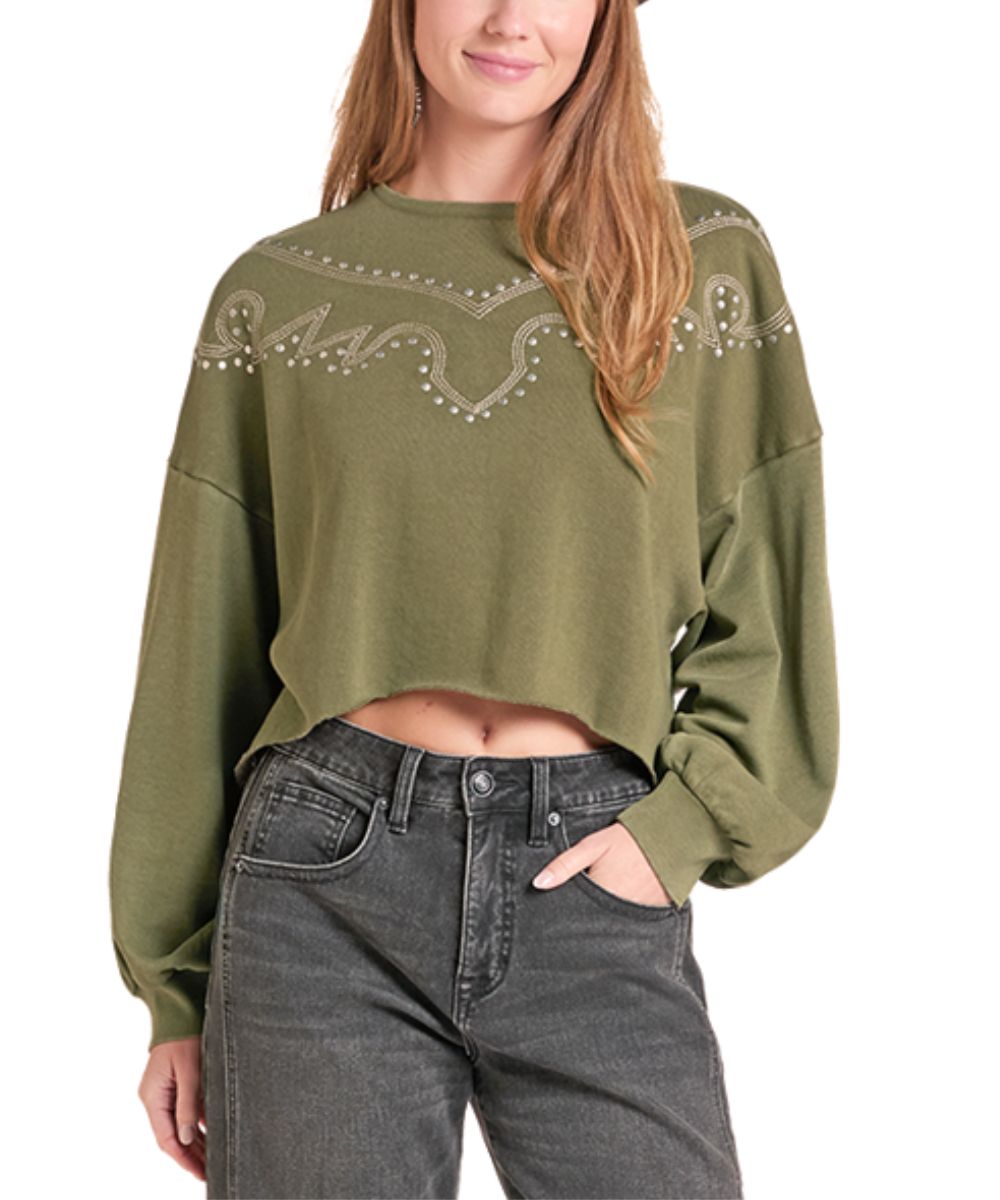 A woman wearing an olive green cropped long-sleeve sweatshirt with a western-style embroidered pattern across the chest, paired with dark gray jeans, against a plain white background.
