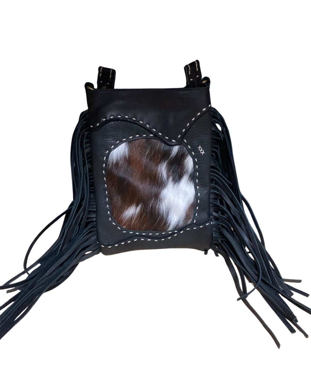 Front view of the women's black Pranee Cheyenne Darby Bag featuring the removable/adjustable crossbody strap, leather construction, hair-on-hide front center inlay, contrast buck stitching, side fringe, and a top zipper closure