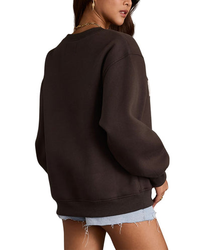 A woman wearing an oversized dark charcoal crewneck sweatshirt, shown from a side-back angle against a plain white background.