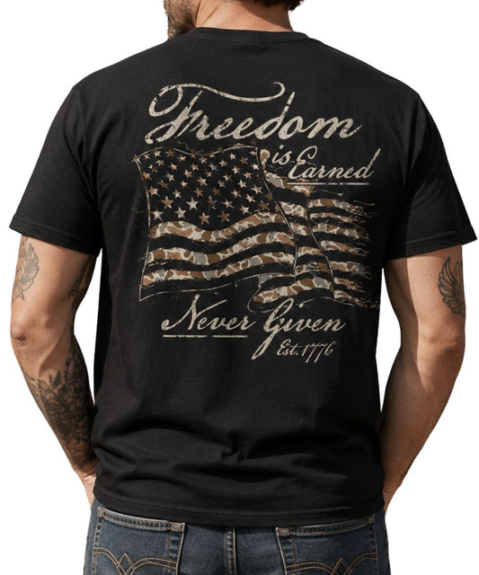 Back view of a man modeling the black tee featuring a large camo printed American Flag graphic that reads: "freedom is earned never given est. 1776"