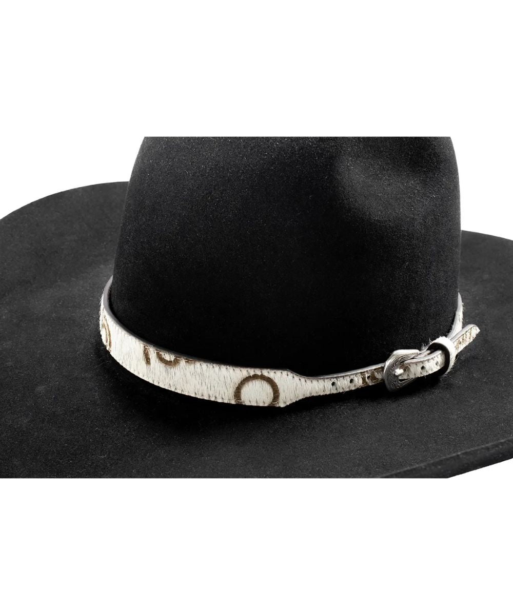A close-up of a black cowboy hat featuring a white western-style band with brown engraved lettering and a silver buckle.
