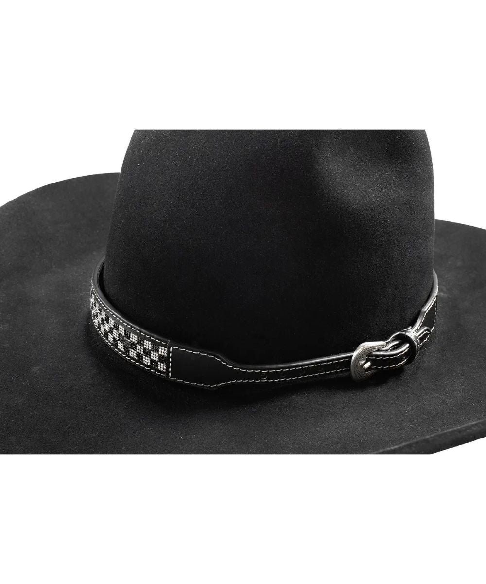 A close-up of a black cowboy hat featuring a decorative black and white checkered leather band with white stitching and a silver buckle.