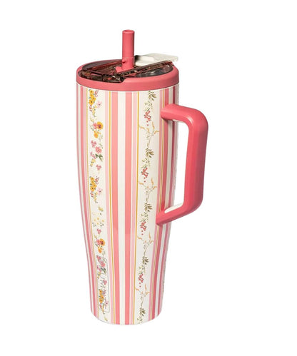 A tall travel tumbler with a pink handle and lid, featuring a vertical pink and cream stripe pattern with delicate floral illustrations, shown on a white background.