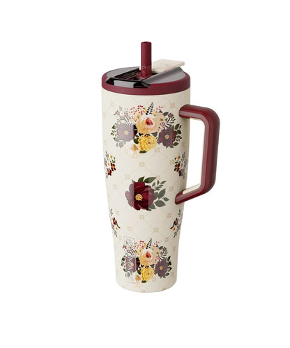 A tall insulated travel tumbler with a floral pattern, featuring a burgundy handle, matching burgundy lid, and a small tea bag resting in the lid.
