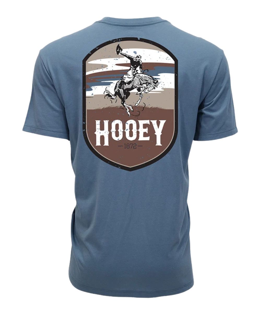 A blue short-sleeve t-shirt shown from the back, featuring a large shield-shaped graphic with a cowboy riding a bucking horse and the word 'HOOEY' in white.
