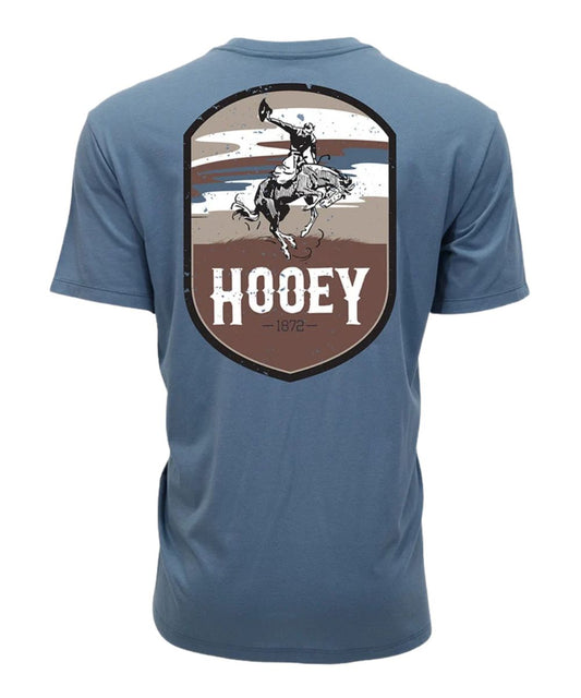A blue short-sleeve t-shirt shown from the back, featuring a large shield-shaped graphic with a cowboy riding a bucking horse and the word 'HOOEY' in white.