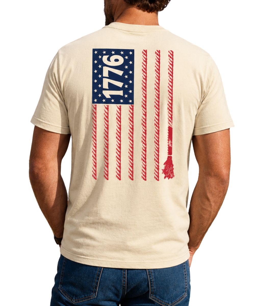 Back view of a man modeling the cream cotton tee featuring a red and navy blue American flag printed on the back with rope stripes and "1776" printed in the stars